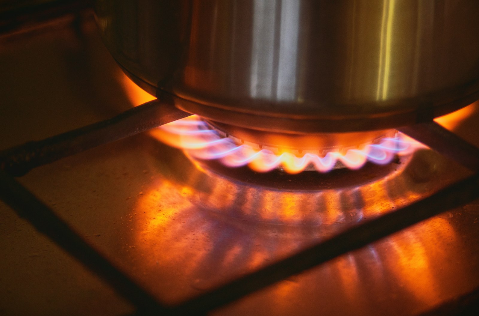 A steel pot heating over the blue and orange flame of a gas burner